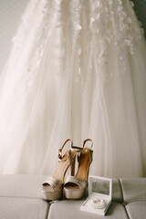 The bride's gold wedding shoes, earrings and a pearl bracelet on the background of the wedding dress.