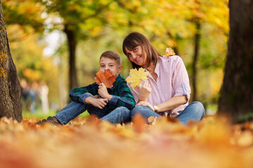 Fototapeta premium Mom and son are sitting on the ground in a beautiful autumn forest. Love and tenderness.