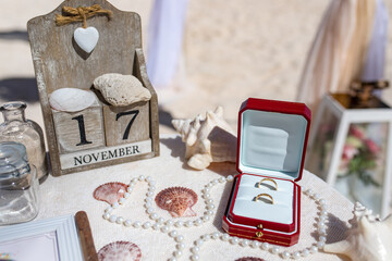 Close up view of wedding rings in the red wooden box on the table with wedding decor at the beach...