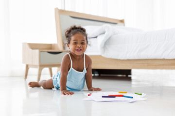 Happy adorable cute African American little girl playing and drawing on floor in living room at home. African American little girl smiling and looking at the camera