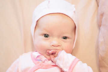 Baby in a pink blouse and cap, sucking fingers on his hand. Close up shot.