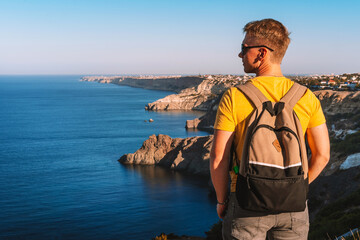 Fototapeta premium Young man with blond hair on vacation on the edge of the cliff of Cape Fiolent in Crimea, beautiful view of the Black sea