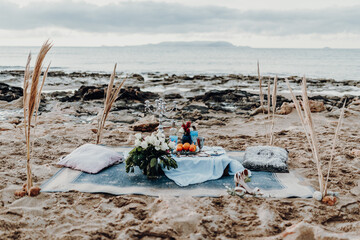 Maritime elegant pastel blue engagement wedding decor picnic on the beach background. Picnic with flowers, fruit, candle holder, vine, seashell. Outdoor ceremony decoration concept. Crete, Greece.