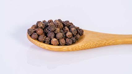 Black pepper corns on bamboo spoon isolated on white background