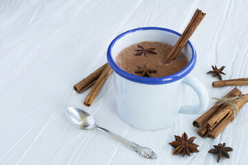 Hot cocoa with cinnamon in the white metal mug  on the white wooden background