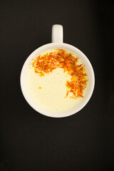 Top view of saffron latte or saffron moon milk in the white cup on the black  background with copy space