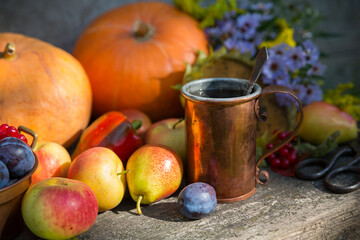 Copper mug with tea against the background of the autumn harvest of pumpkins, apples, plums, pears and viburnum on a wooden table. Vintage rustic style