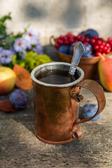 Copper mug with tea on a wooden old table with viburnum berries, plums, apples. Autumn still life in a rustic style.