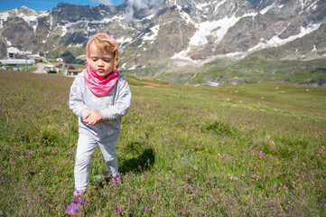 Naklejka na ściany i meble Cute blonde girl wearing pink scarf surrounded with spectacular alpine scenery exploring mountain meadow.