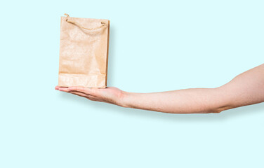 Paper bag in hand on a blue pastel background. Concept of using ecological items. The man holds a brown bag with a gift, purchases in his hand. Giving gifts.
