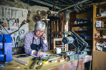 Senior female carpenter talking on the phone in her workshop
