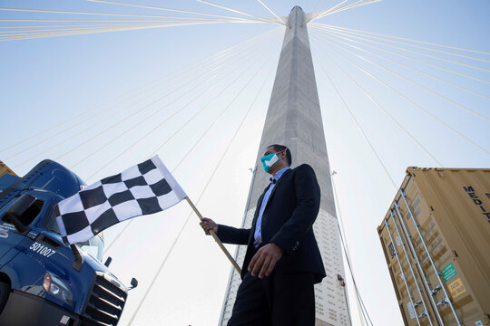 Mayor of Long Beach Robert Garcia wears a protective face mask while waving a checkered flag at the reopening ceremony for the Gerald Desmond Bridge in Long Beach