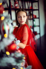 
girl in a red dress decorates a Christmas tree
