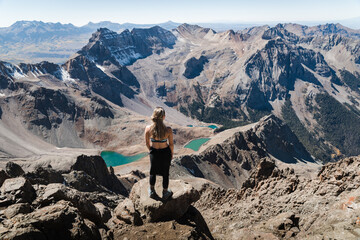 A woman standing at the summit of Mount Sneffles enjoying the view of the Blue Lakes. 