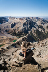 A woman sitting at the peak of Mount Sneffles with the Blue Lakes in the distance. 