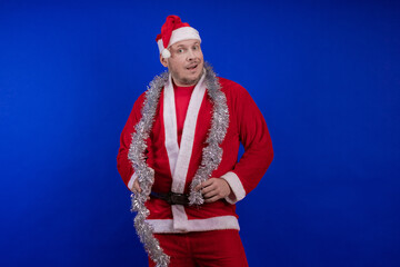 Male actor in a suit and hat of Santa Claus with a silver tinsel garland dancing and posing on a...