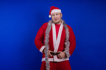 Male actor in a suit and hat of Santa Claus with a silver tinsel garland dancing and posing on a...