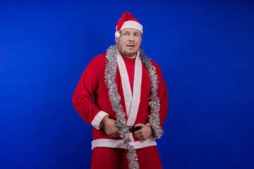 Male actor in a suit and hat of Santa Claus with a silver tinsel garland dancing and posing on a...