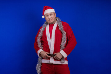 Male actor in a suit and hat of Santa Claus with a silver tinsel garland dancing and posing on a...