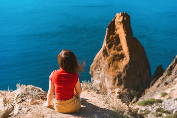 Rear view of traveler woman standing on cliff edge in front of amazing seascape. Freedom, travel and vacation concept.