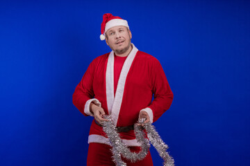 Male actor in a suit and hat of Santa Claus with a silver tinsel garland dancing and posing on a...