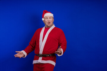 Male actor in costume and hat of Santa Claus posing on a blue background.