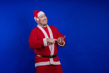 Male actor in costume and hat of Santa Claus posing on a blue background.