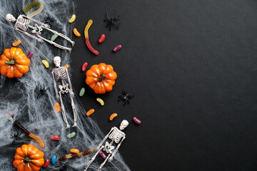Happy halloween holiday concept. Halloween decorations, skeletons, pumpkins, candies, spider web on black background. Halloween party greeting card mockup with copy space. Flat lay, top view, overhead