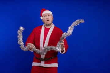 Male actor in a suit and hat of Santa Claus with a silver tinsel garland dancing and posing on a...