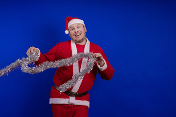 Male actor in a suit and hat of Santa Claus with a silver tinsel garland dancing and posing on a...