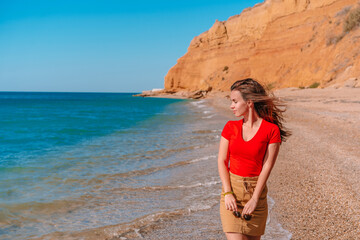 Charming brunette woman walks along the beach and admires the azure clear sea water, relaxing on the Black sea