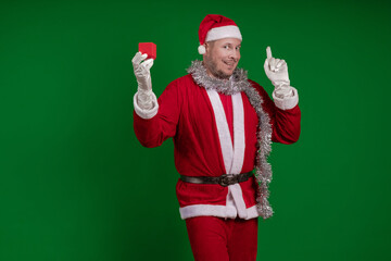 Emotional male actor in a costume of Santa Claus holds a small red gift box in his hands and poses...