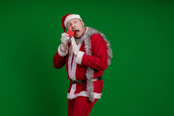 Emotional male actor in a costume of Santa Claus holds a small red gift box in his hands and poses...