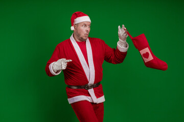 Emotional male actor in a costume of Santa Claus holds a Christmas sock for gifts in his hands and...