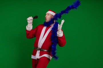Emotional male actor in a costume of Santa Claus and a blue garland of tinsel holds a microphone in...