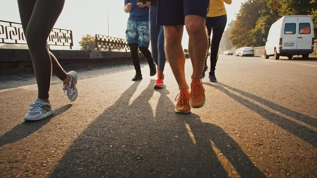 Close up of sporty people legs running on sidewalk early in morning, slow motion
