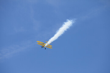 Bright yellow biplane flying up in the sky with white smoke trail behind