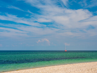 beach view to calm sea with alone red board sailing yacht under blue sky with copy space