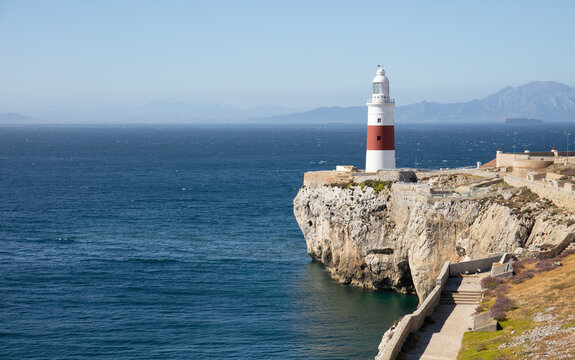 The red and white lighthouse of Gibraltar in sunshine in June. The Strait of Gibraltar and the mountains of the Spanish south coast can be seen in the background.