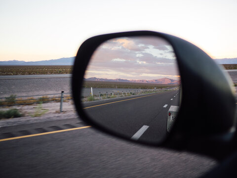 Sunset and mountains in side view mirror while driving on road trip