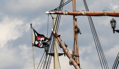 A skull and cross bones pirate flag flying from the rigging of a tall ship replica in St Augustine,...