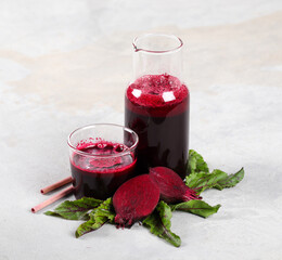 Beetroot drink cocktail in a bottle and glass with a bamboo straw on a light gray background