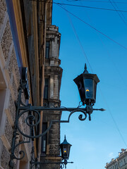 Fototapeta na wymiar Old vintage black dark glass street lanterns hanging on textured wall of beautiful building in city of Saint Petersburg. Blue sky gradient. Ancient architecture