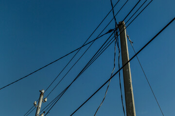 Fototapeta premium Power lines, electric poles with black straight wires on blue sky background