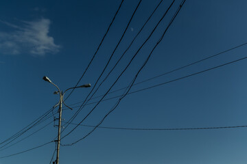 Ordinary city lamppost with three glass lamps. Black wires all around. Evening blue sky gradient  background with white moon and cloud