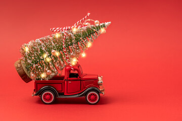 Red small retro toy truck with sparkling Christmas tree lights on truck body on red background....