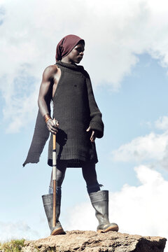 A Portrait of a young black Basotho shepherd standing against a clouded sky.