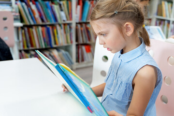 Little girl reads book with fairy tales in children's library. Special reading kids room. Many...