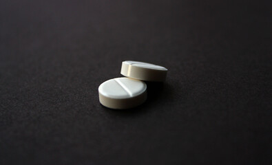 Two white medium sized pills on the black rough paper background.