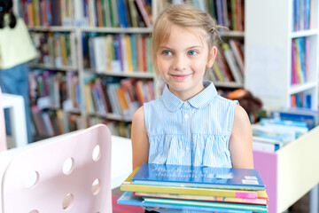 Little girl holds stack of books with fairy tales in children's library. Special reading kids room....